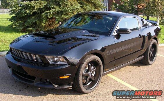 Black Ford Mustang with racing stripes on hood, aftermarket wheels, and hood scoop