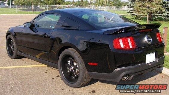 Black Ford Mustang coupe with a rear spoiler and black rims, parked in a lot