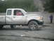 1993 Suzuki Sidekick - A damaged silver pickup truck sits in a sandy area with a child standing nearby.