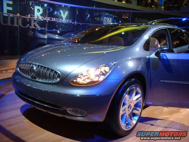 Front 3/4 view of a silver Buick concept car with its driver's door open, on display indoors