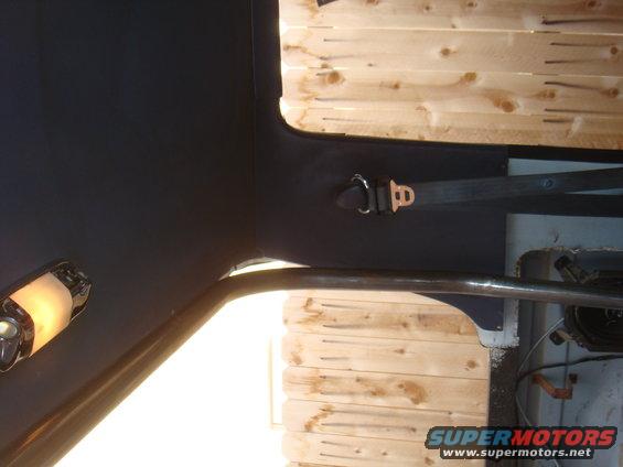 Interior view of a vehicle showing a seatbelt and roll cage against a wood-paneled background