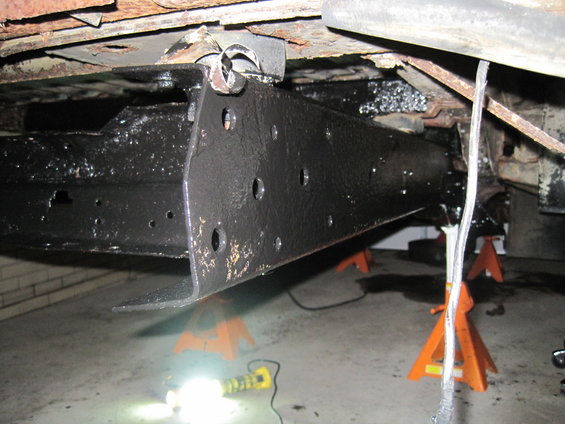 Vehicle frame and suspension parts on jack stands, with black undercoating and rust visible