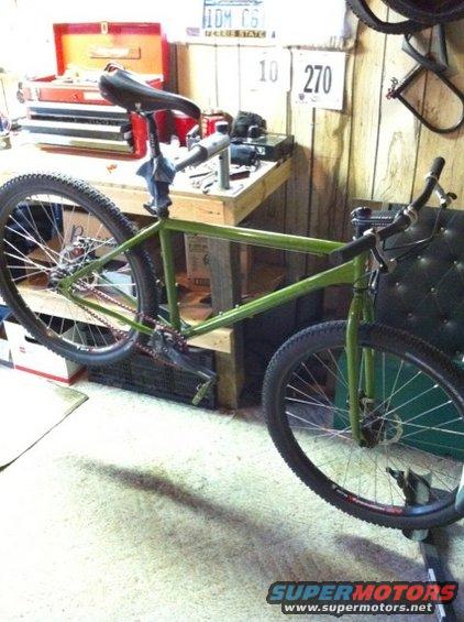 Green bicycle frame with wheels and handlebars, held on a workbench