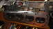 1964 Ford Fairlane - A disassembled engine cylinder head sits on a shelf with other automotive parts, including a chrome grille.