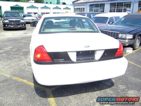Rear view of a white sedan parked in a lot. Other vehicles are visible