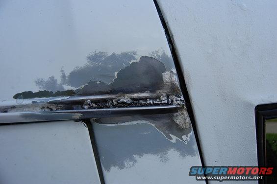 Close-up of rust and peeling paint on a vehicle's body panel, with visible weld marks