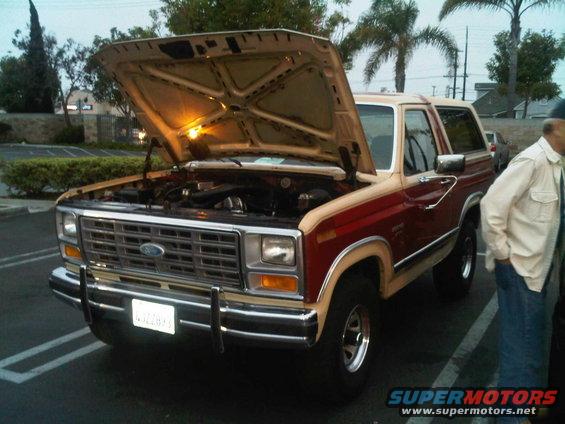 Ford Bronco with hood open, showing engine. Two-tone red and tan paint. Person standing next to it