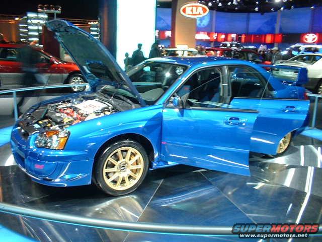Blue Subaru Impreza WRX STI with hood and driver door open, gold wheels, at an auto show