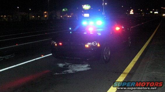 Black police car with flashing blue and red lights, front view, parked on a road at night