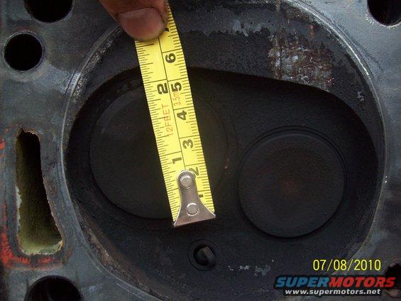 Engine cylinder head with two valve openings, a yellow measuring tape across one opening, and a date stamp of 07/08/2010