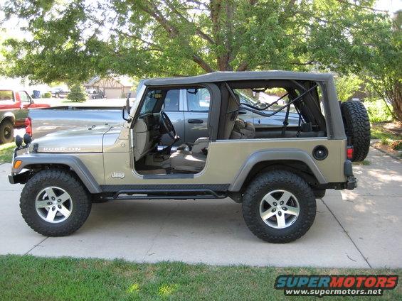 Tan Jeep Wrangler Rubicon parked outside, doors off, with a silver pickup truck behind it