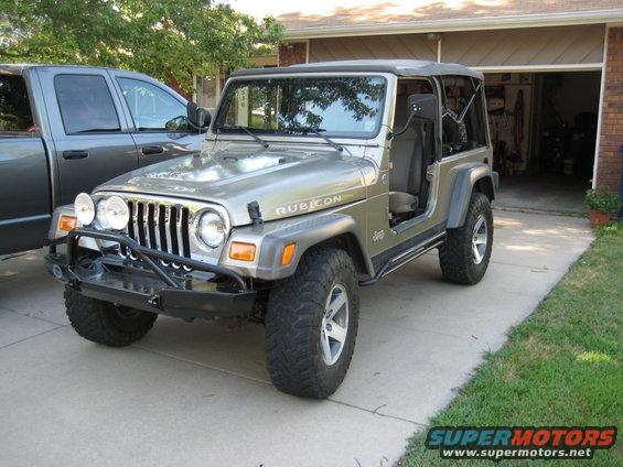 Silver 2005 Jeep Wrangler Rubicon with aftermarket bumper and off-road tires parked next to a gray pickup truck