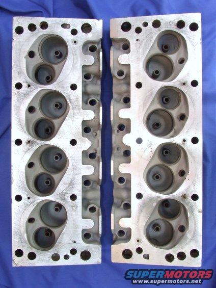 Two aluminum engine cylinder heads with intake and exhaust ports, laid flat on a blue surface