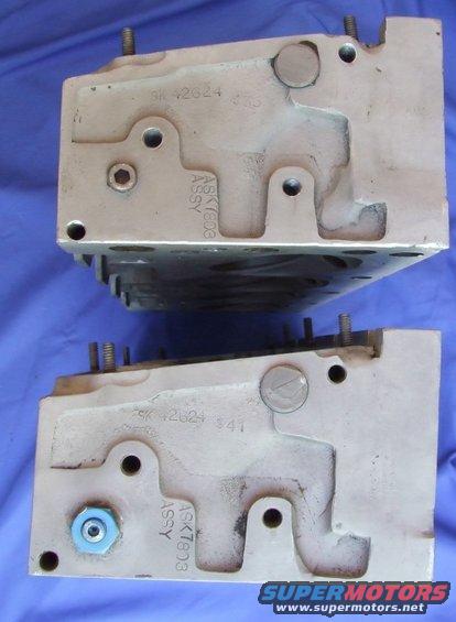 Two beige engine cylinder heads with visible casting numbers and ASSY markings