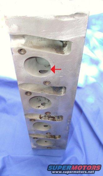Aluminum engine cylinder head with multiple ports and a red arrow pointing to one of the openings