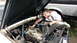 1964 Ford Fairlane - A person works on the engine of a car, with another vehicle parked behind it.