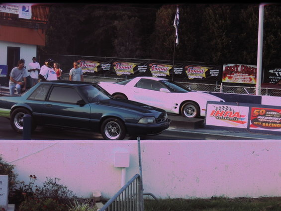 Dark green coupe and white coupe at drag strip starting line, people watching