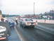 1992 Ford Mustang - A drag racing car is on the track, with a person leaning over its side. Spectators watch from the stands.
