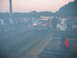 1992 Ford Mustang - A red drag car creates a cloud of smoke during a burnout on a race track as spectators watch.