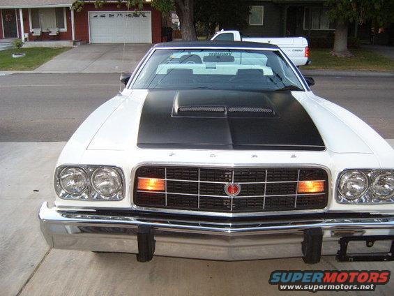 White Ford Ranchero with black hood scoop and grille. White pickup truck in background