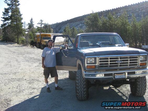 Man by lifted 1980s Ford F-Series truck; two yellow dump trucks in background