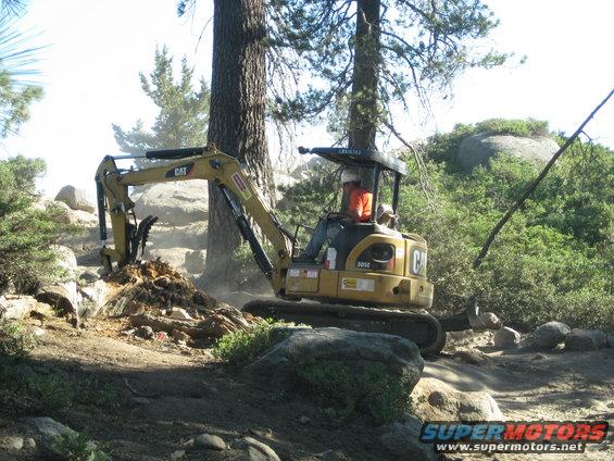 Yellow CAT mini excavator digging dirt and rocks on a sunny day