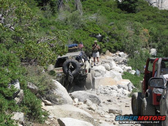 Tan SUV with spare tire on rear, navigating a rocky mountain trail