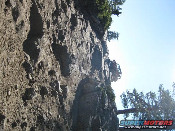 Off-road vehicle parked on a steep cliff face with trees and sky in background