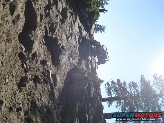 Off-road vehicle on a steep, rocky incline under a clear blue sky