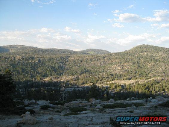 Rocky terrain and forested mountains under a partly cloudy sky