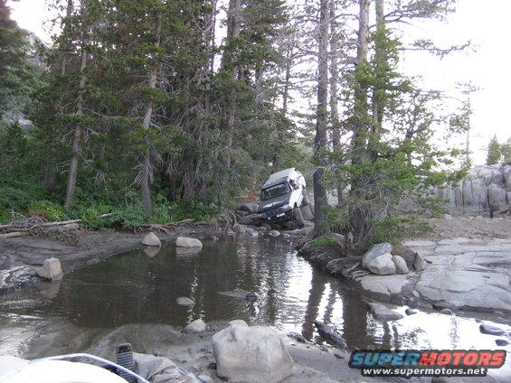 White 1986 Ford Bronco driving through water and rocks