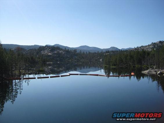 Lake with a line of buoys and forested mountains under a clear blue sky
