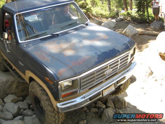 Old Ford truck with rusty hood on rocky trail. Driver visible inside