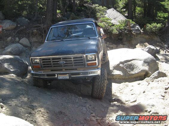 Dark blue 1980s Ford Bronco navigating a rocky off-road trail