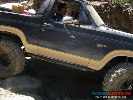 Dark blue and tan Ford Bronco with off-road tires navigating rocks