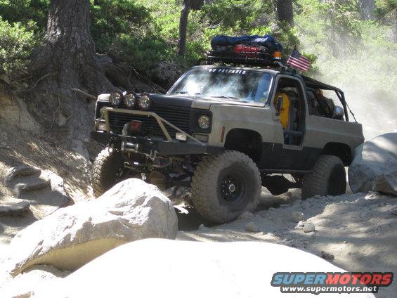 Tan and black off-road SUV with roof rack and winch, navigating rocks
