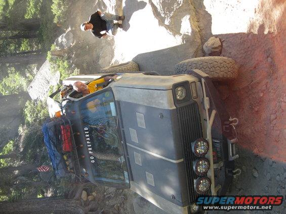 Off-road vehicle stuck on a rocky trail with two people nearby