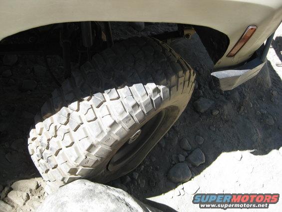 Off-road tire on a light-colored vehicle, angled over rocks