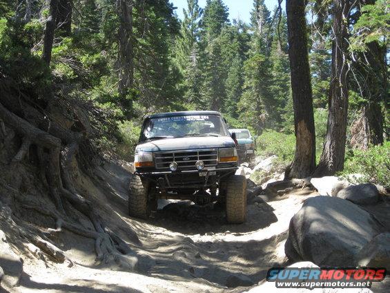Green Ford Bronco on a rocky trail, another vehicle behind it