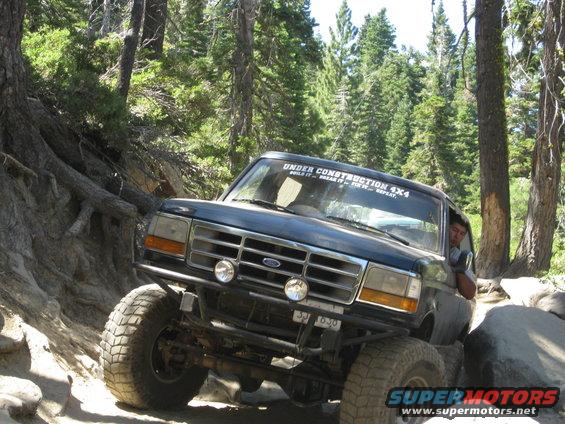 Dark blue 1992 Ford Bronco navigating rocky terrain with "Under Construction 4x4" sticker on windshield