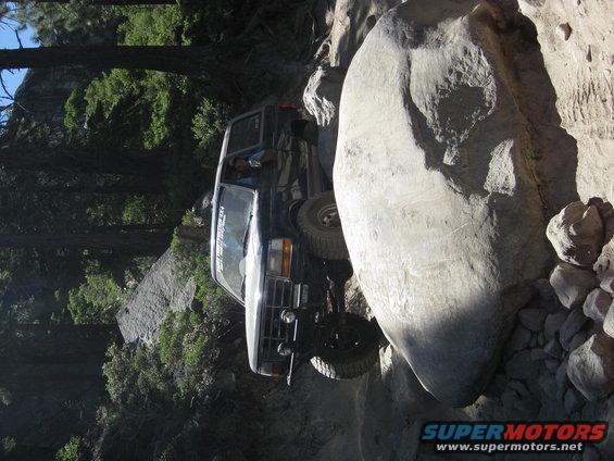 Black SUV navigating a tight spot between large rocks on a trail. Driver visible