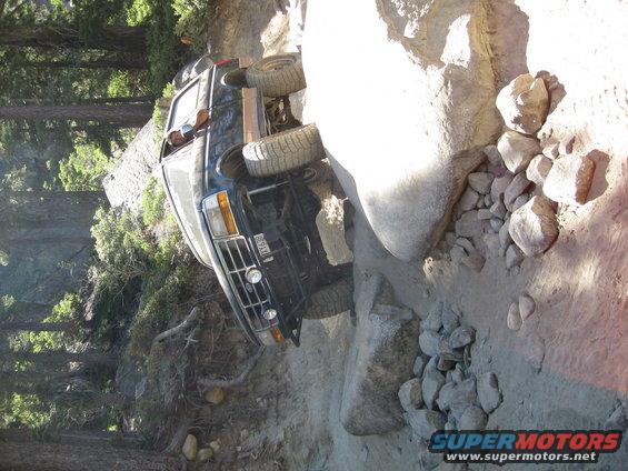 Black SUV on its side, front grille and headlights visible, tires stuck in rocks