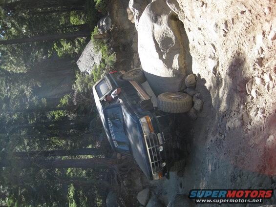 Dark blue SUV wedged between rocks on a steep trail. Driver's side door is open