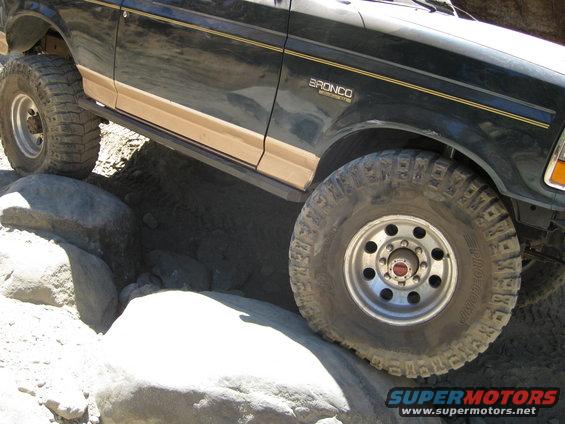 1986 Ford Bronco side view, front wheel on rock, dark green paint with tan trim