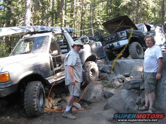 1986 Ford Bronco with kayak on roof rack next to another off-road truck with hood open