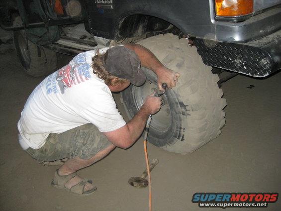Man airing up a large off-road tire on a vehicle. A tool is connected to the valve stem