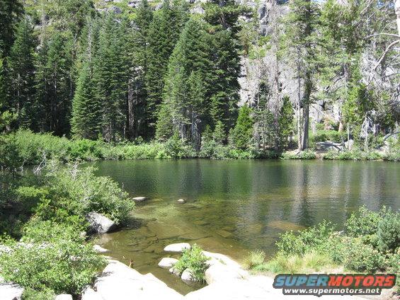 Lake with clear water and rocky shore, surrounded by pine trees and granite cliffs