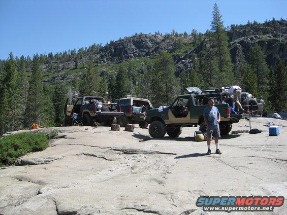 Green and tan Ford Bronco parked on rocky terrain with people loading gear