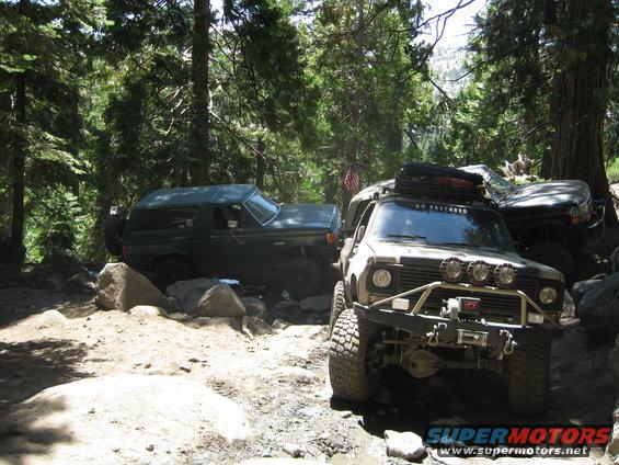 1986 Ford Bronco and another off-road vehicle navigating a rocky trail in a forest