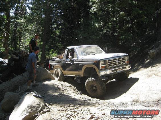 1986 Ford Bronco on a rocky, wooded trail with two men standing nearby